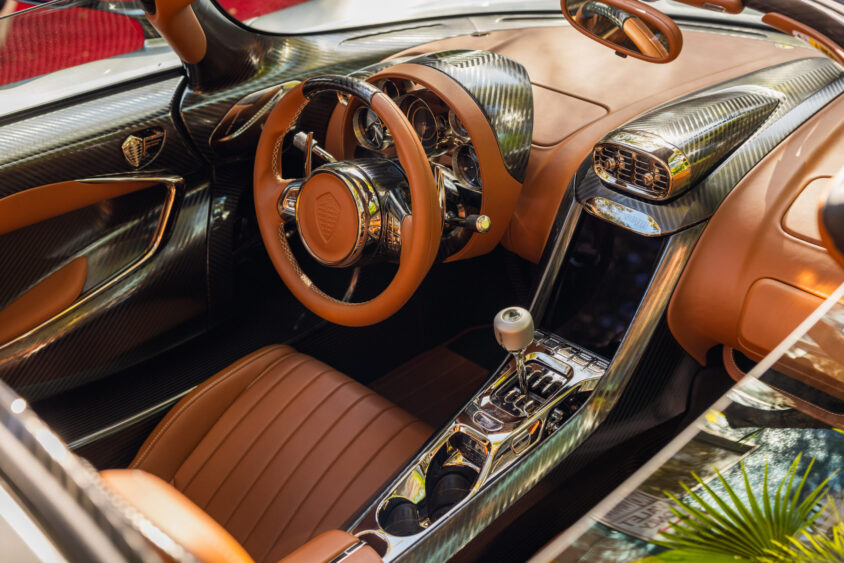 Luxury sports car interior featuring brown leather seats, a sleek carbon fiber dashboard, modern controls, and a polished metal gear shifter—each element Driven By Design and elegantly illuminated by natural sunlight. Lifestyle